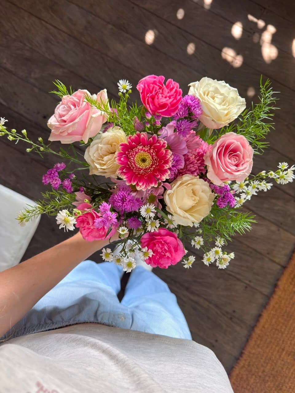A hand holding a bouquet of roses, gerberas and small white daisies