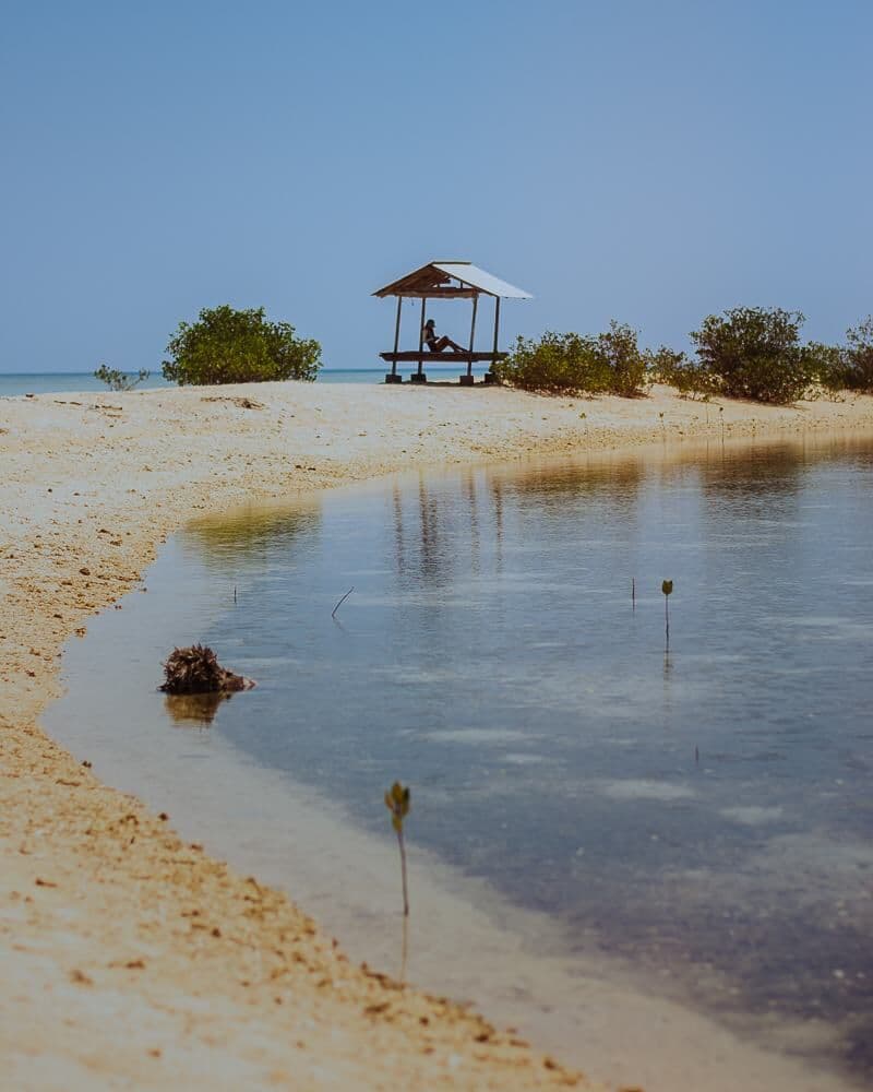 A white sand beach on Gili Putih with a small shade hut and shallow water in front