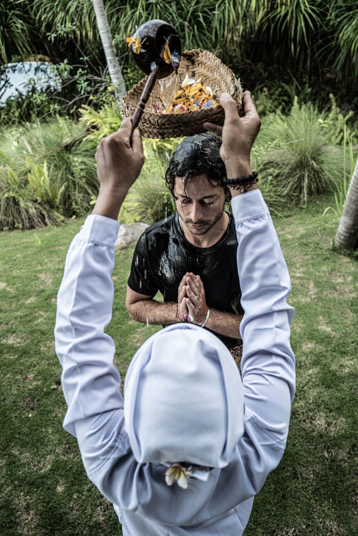 A priest in white pouring water over a man who holds his hands together in prayer