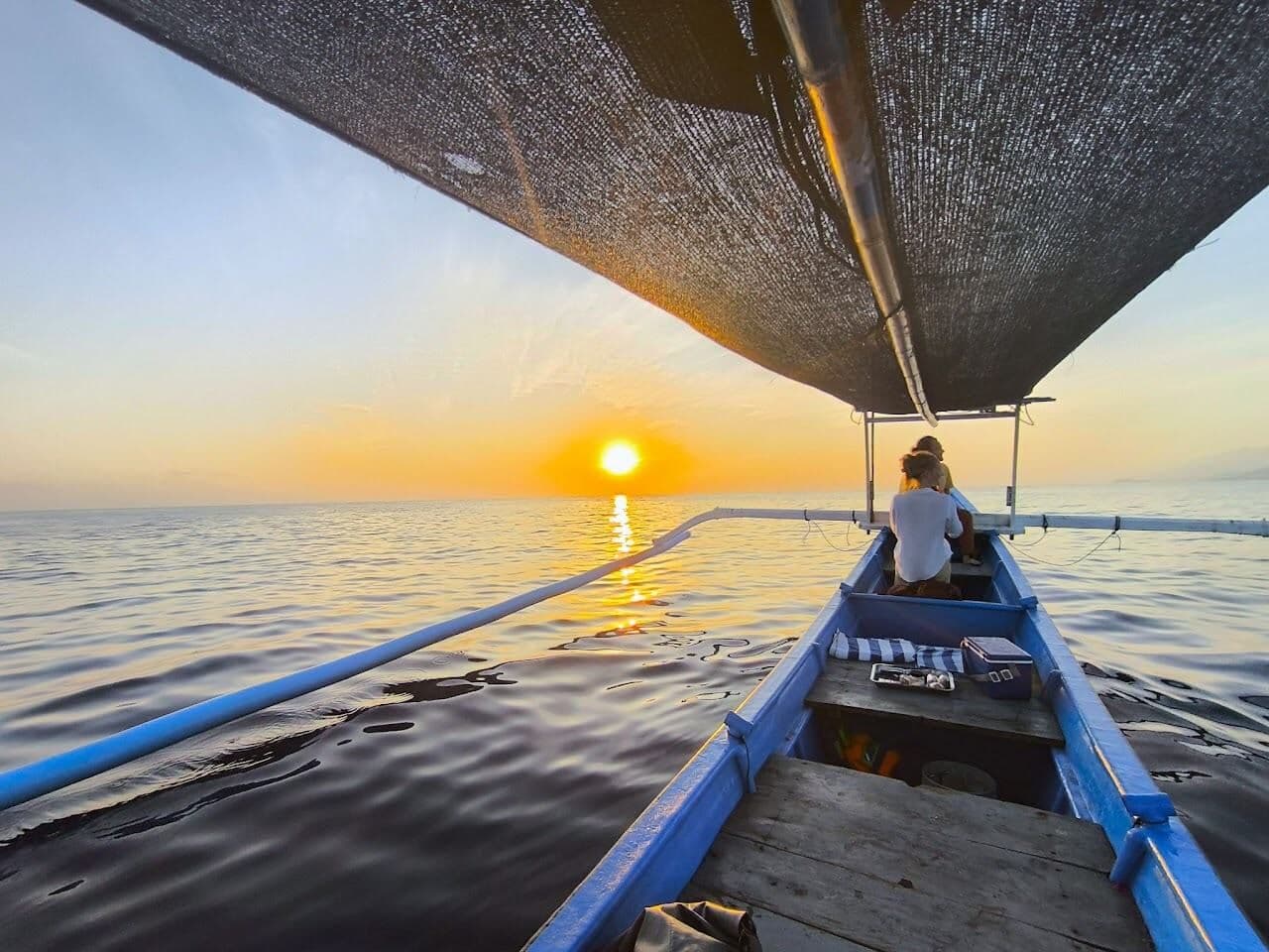 A guest sitting in a traditional outrigger boat under a shade cloth, heading towards the sunrise over the sea