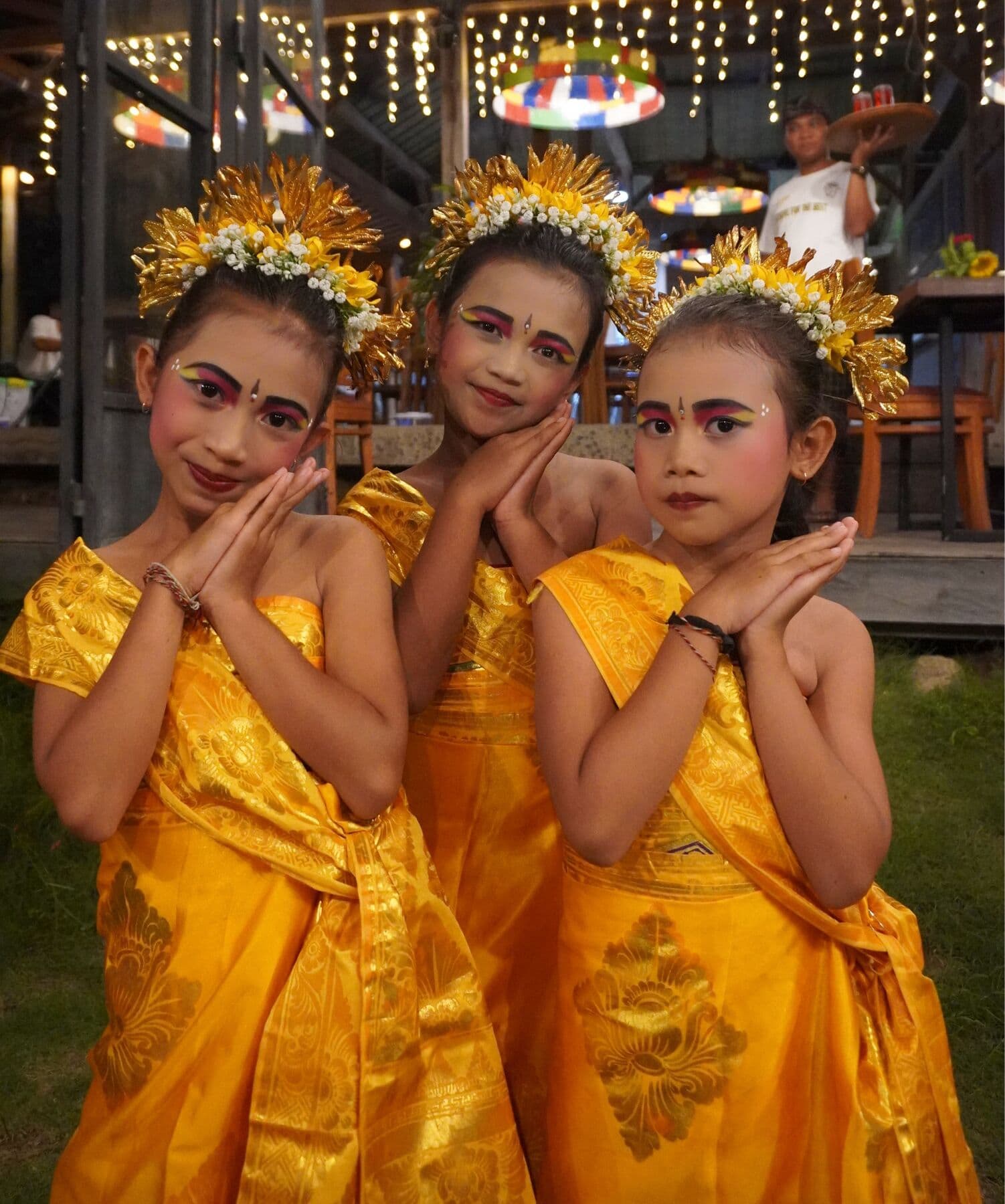 Three young Balinese dancers in gold costumes and flower headdresses