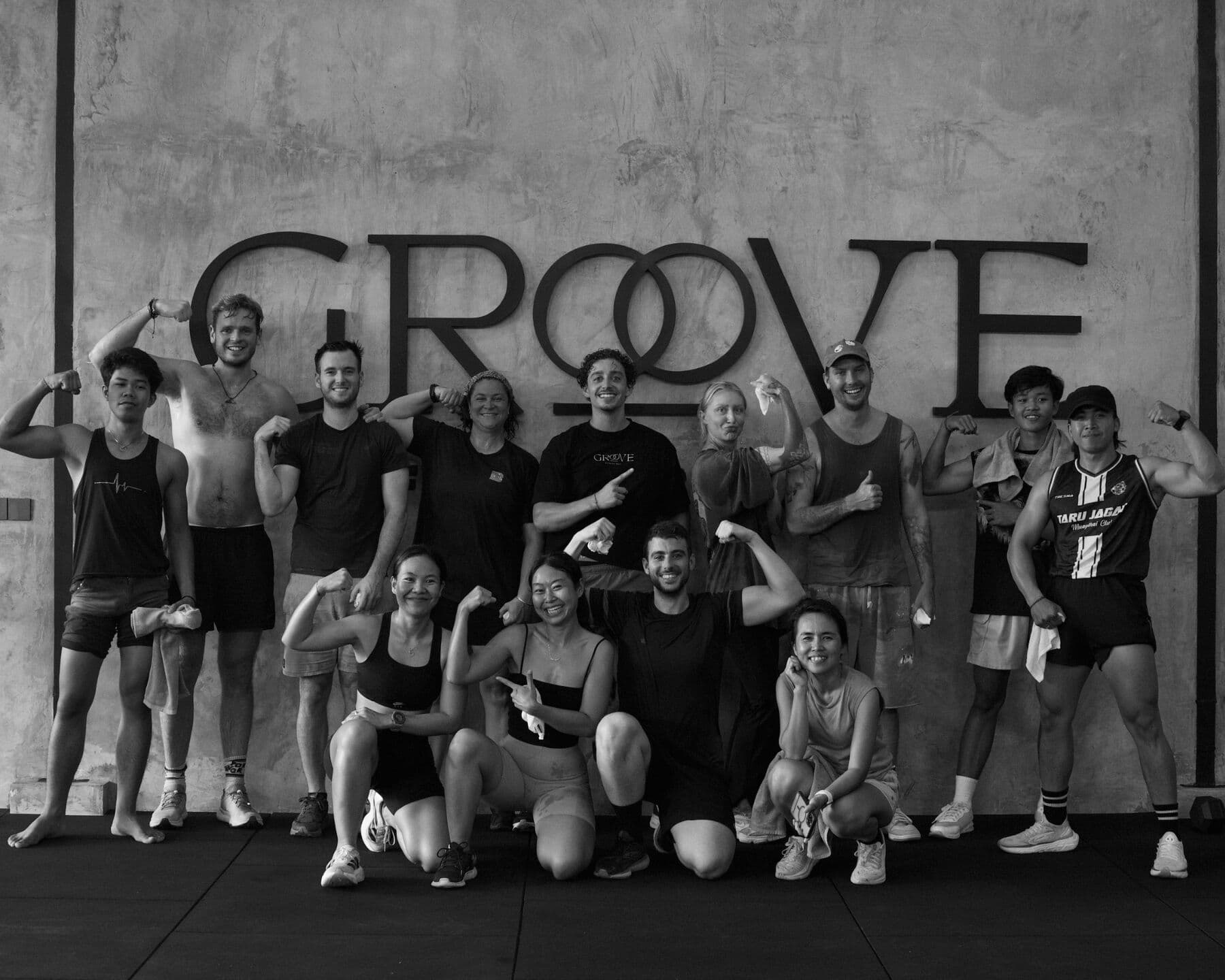 A black and white group photo of people flexing their arms in front of the Groove sign