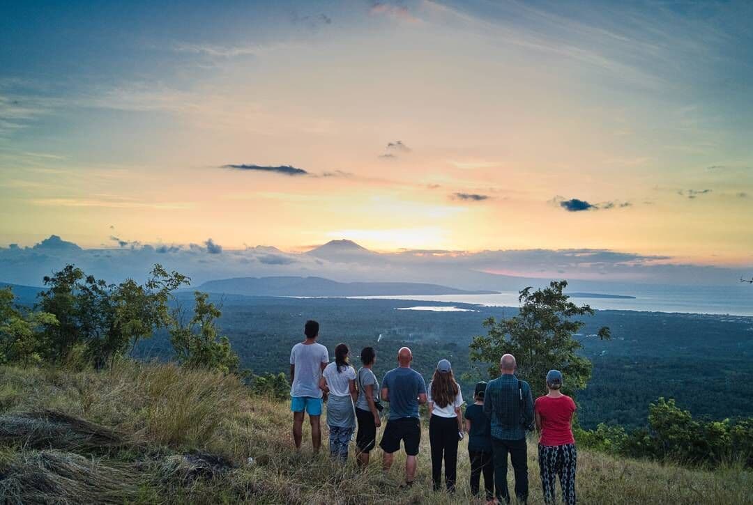 A group of hikers on a hilltop watching the sunrise over the bay