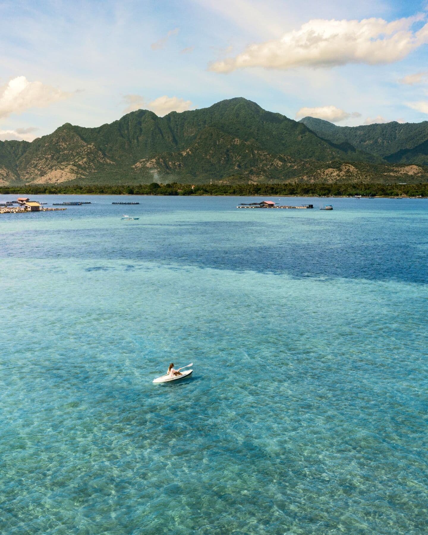 Aerial view of a kayak on clear turquoise water in Sumberkima Bay, with fish farms and mountains behind