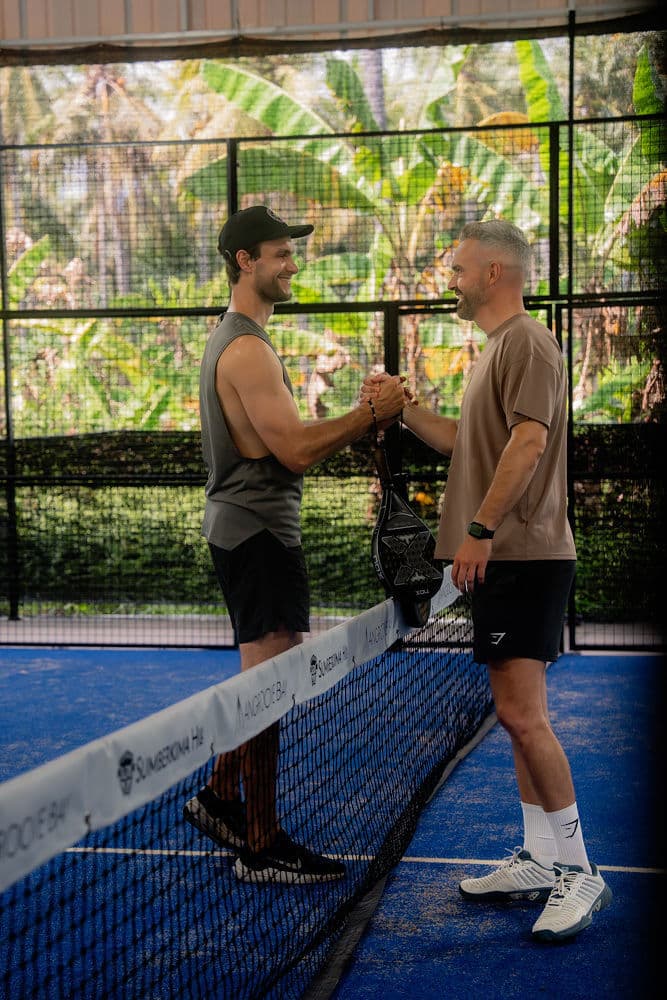 Two men shaking hands over the net on a blue padel court