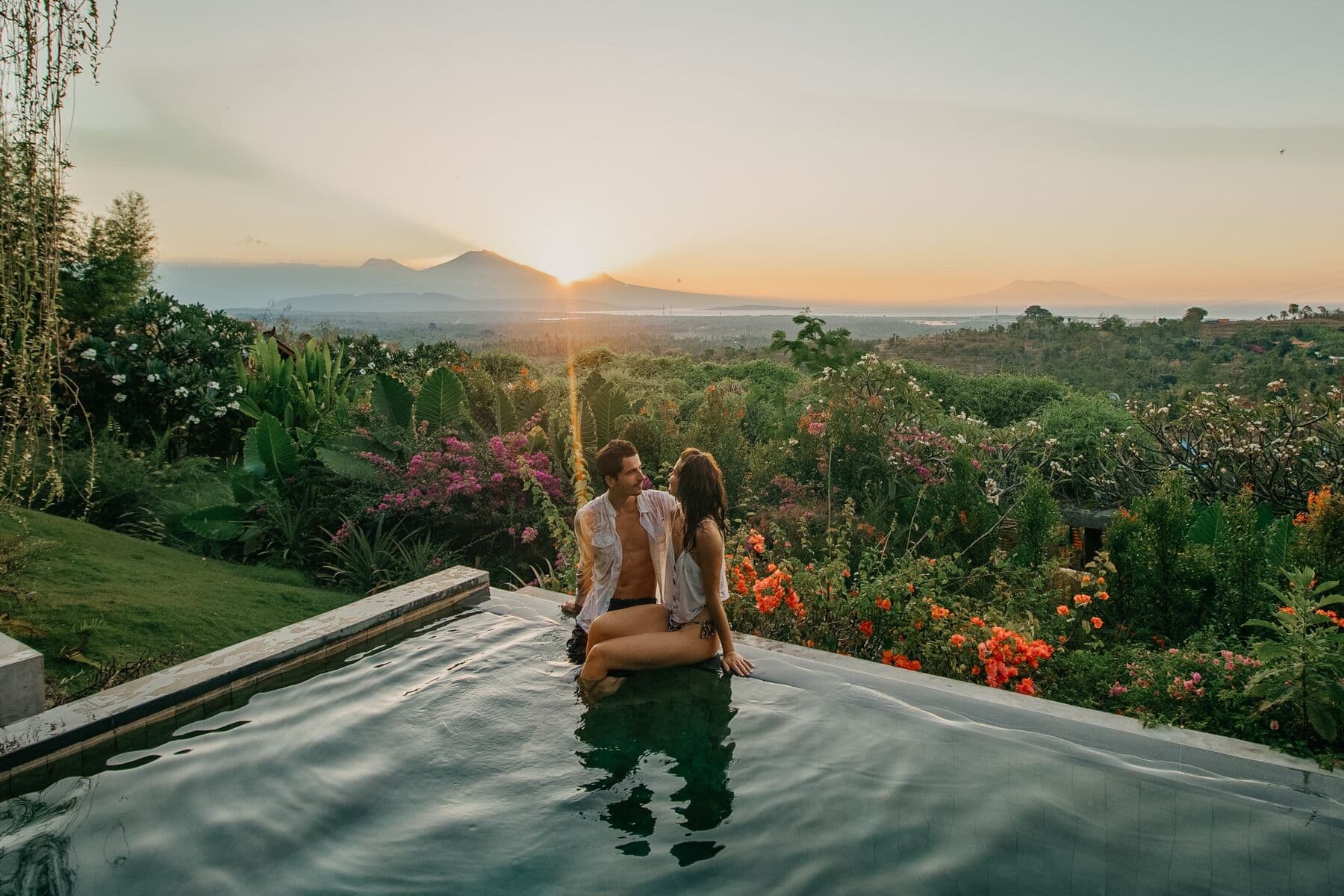 A couple sitting on the edge of an infinity pool at sunset, looking at each other