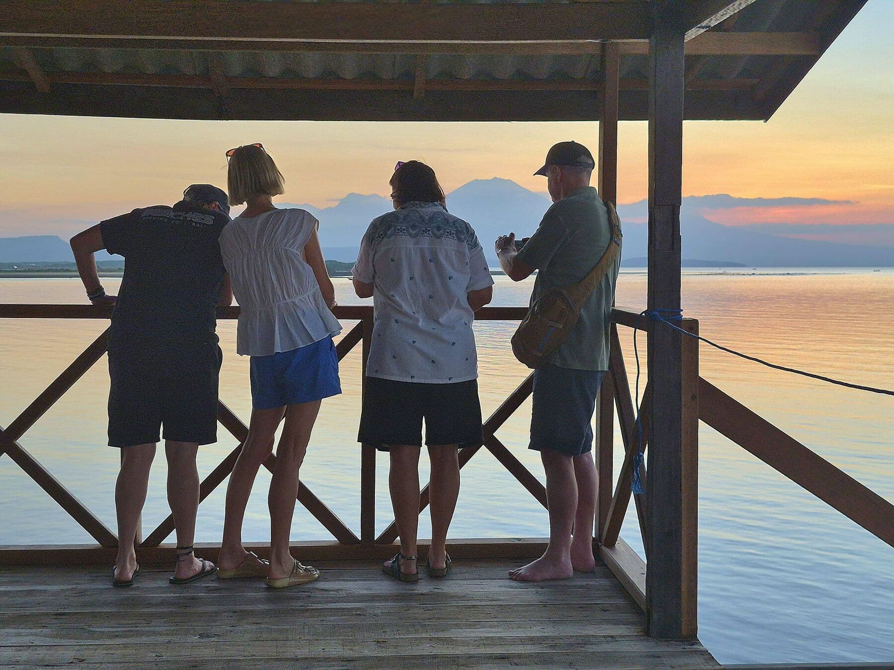 Four guests leaning on the outpost railing, looking out over the bay at sunset