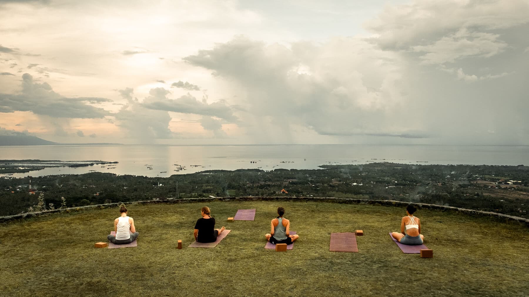 Four people sitting on yoga mats on the grass stage, looking out over the bay