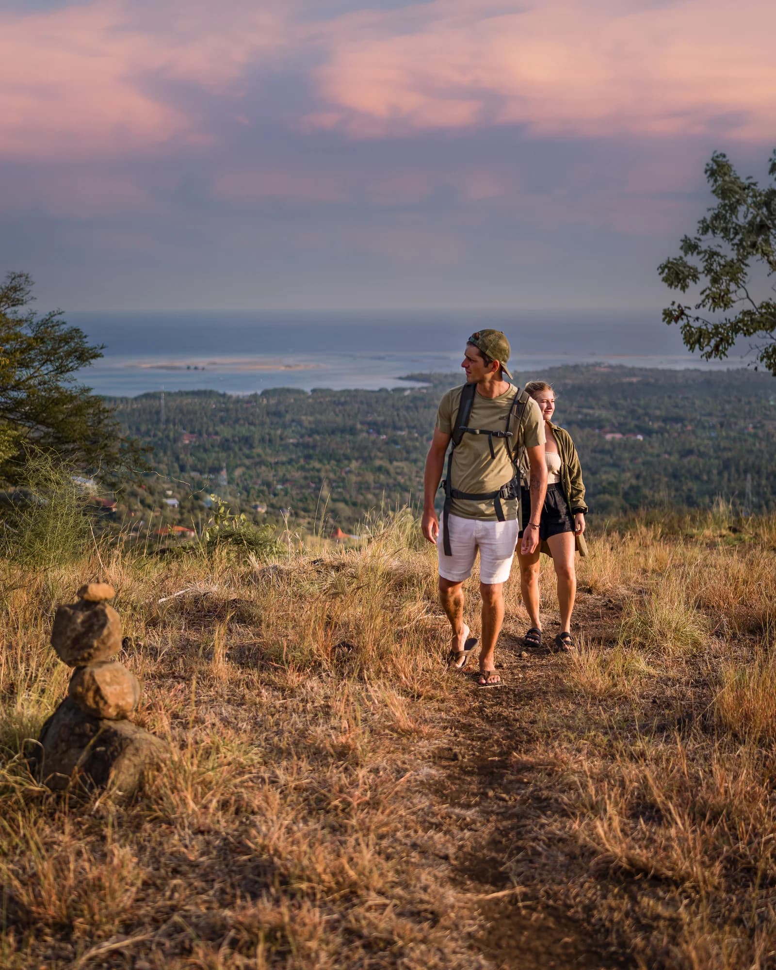Two guests walking on a trail on the hills of Sumberkima with the sea behind them